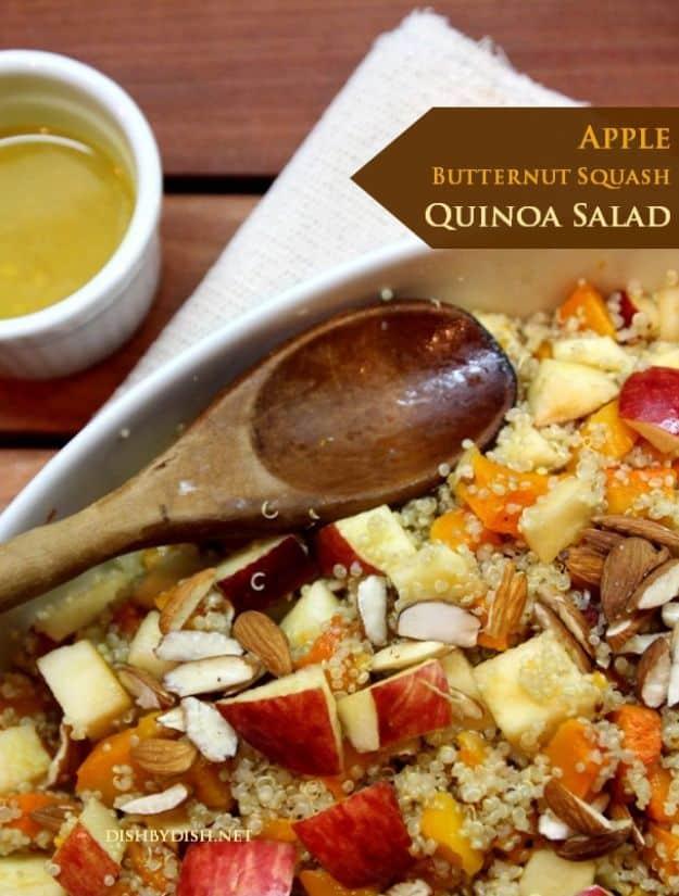 Apple butternut squash quinoa salad close up with a wooden spoon, crumbled feta, almonds and a dressing pot