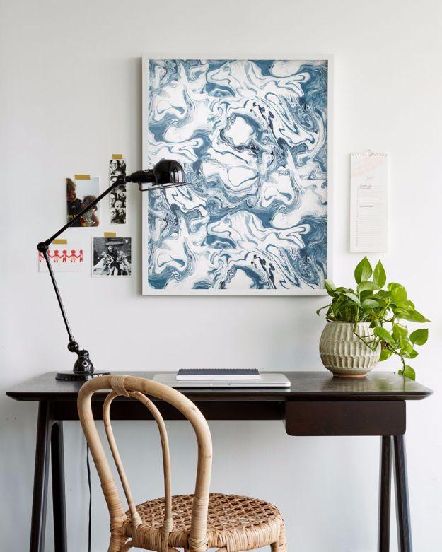 An affordable wallpaper trick, a large framed panel of blue and white marbled wallpaper hung above a dark wood desk and lamp