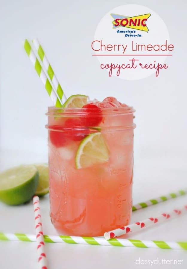 Pink cherry limeade in a mason jar with a lime wheel, maraschino cherries and green and red striped straws