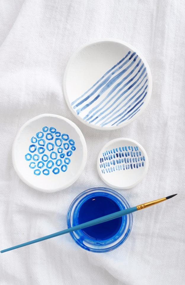 Hand painted indigo clay bowls, four small white clay dishes painted with blue stripes, rings and dashes beside a paint pot