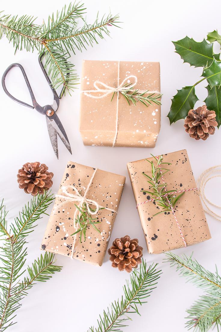 Three kraft paper parcels splatter painted in black and white, tied with twine and topped with rosemary sprigs