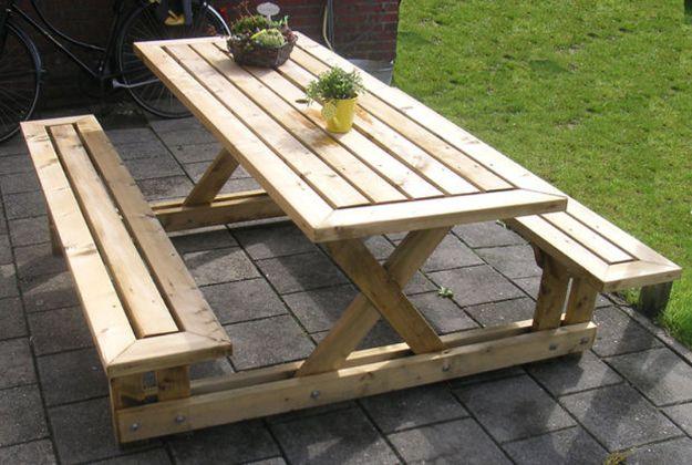 DIY picnic table in pale wood with attached benches and X legs on a paved yard with two small potted plants