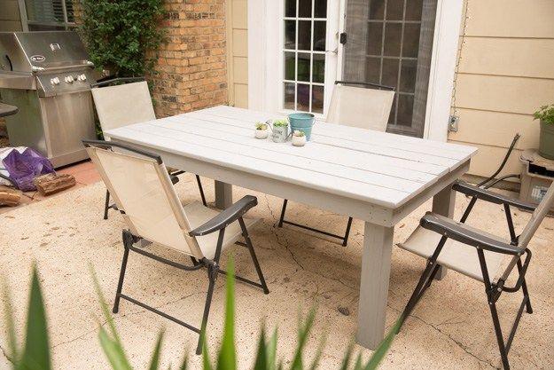 DIY farmhouse patio table painted soft white with four folding sling chairs on a concrete patio by a grill