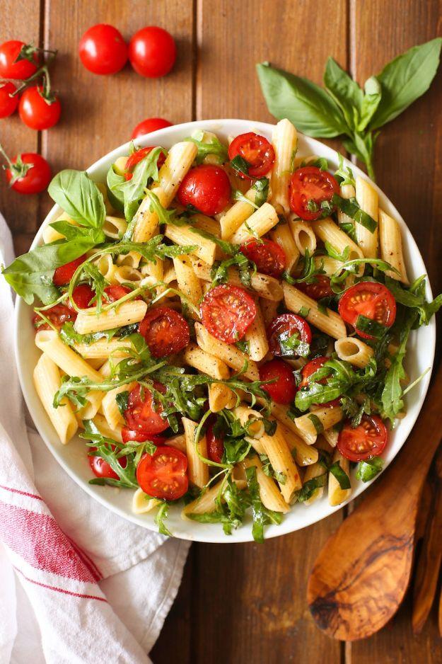 Gluten free penne pasta salad with halved cherry tomatoes and arugula in a white bowl on a wooden board