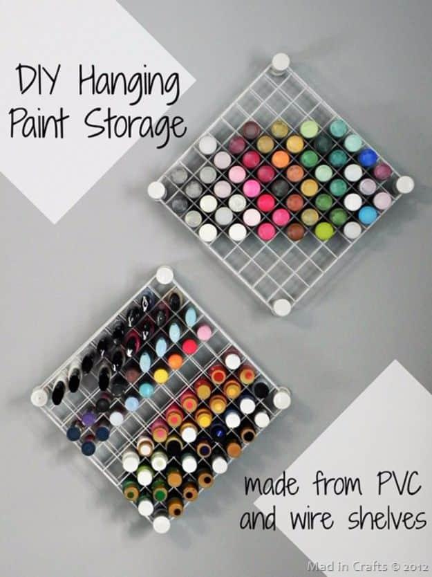 Two wire grid paint racks hung diagonally on a grey wall, each square holding a craft paint bottle sorted by color