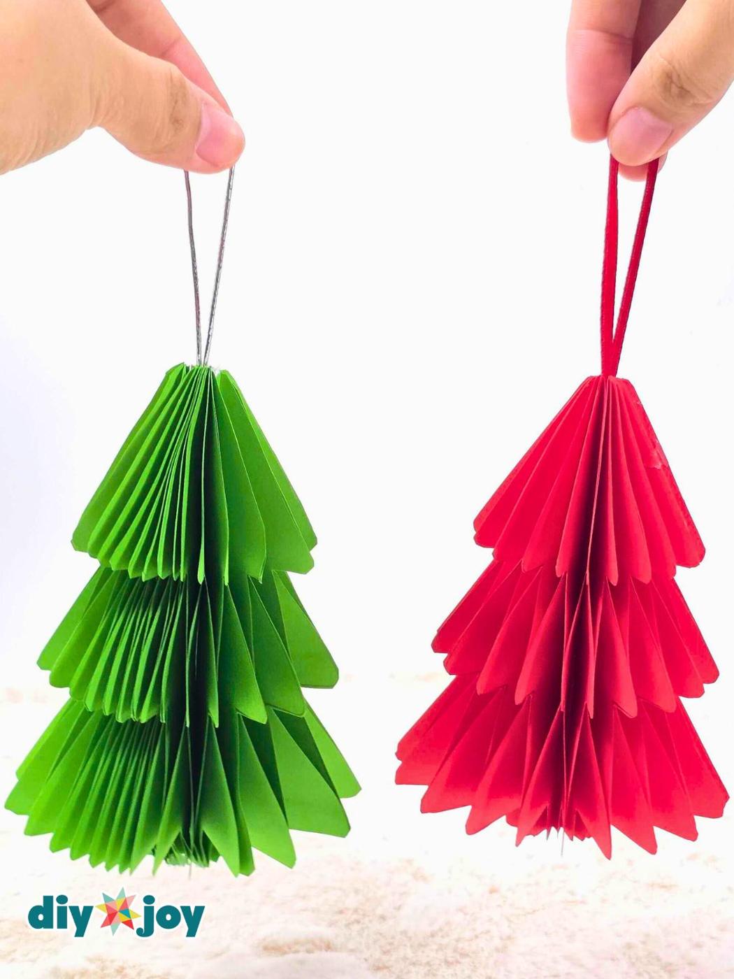 Green and red honeycomb paper Christmas trees with ribbon hanging loops held up against a white background