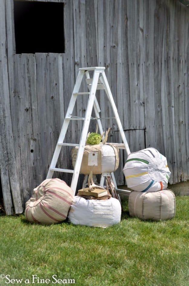 Cylindrical grain sack poufs in cream linen with faded red and blue stripe bands stacked beside a wooden barn