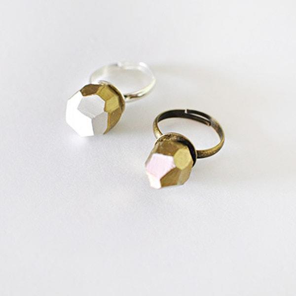 Two geometric faceted clay rings in white and blush pink with gold painted edges on adjustable bases, on a white surface