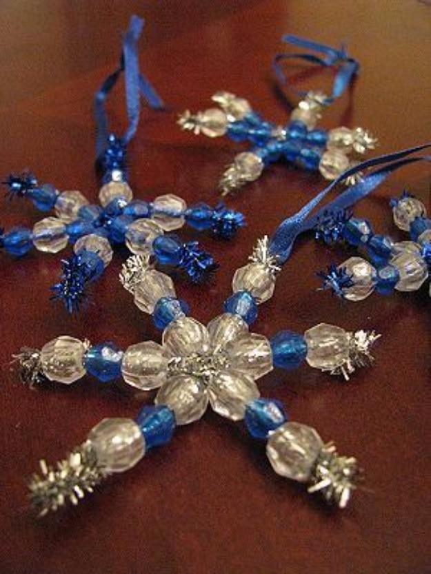 Three beaded snowflake ornaments made from silver pipe cleaners and clear blue beads with ribbon hangers