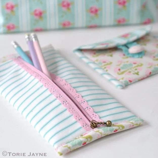 A flat zip pencil case in floral cotton with cream lace trim stitched across the front, resting on a cutting mat