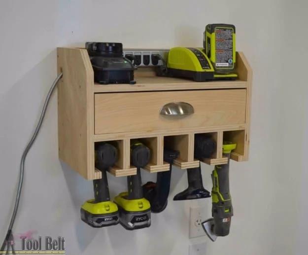 Plywood wall station holding five cordless drills in slots with batteries and chargers above a drawer