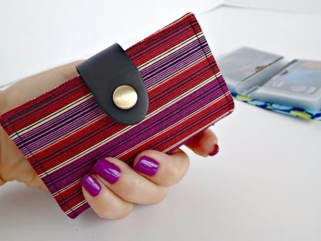 A slim fold-over fabric wallet in a busy woven print with a leather tab and brass snap, holding a stack of cards