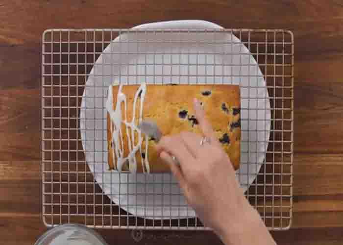 Drizzling the lemon glaze over the blueberry bread
