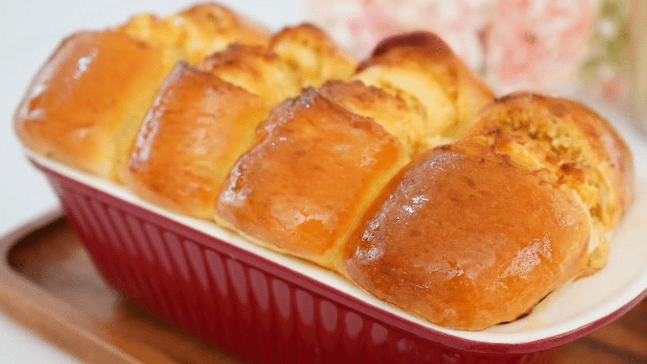 Coconut dream loaf baked whole as five glossy golden pull-apart rolls in a deep red fluted ceramic dish
