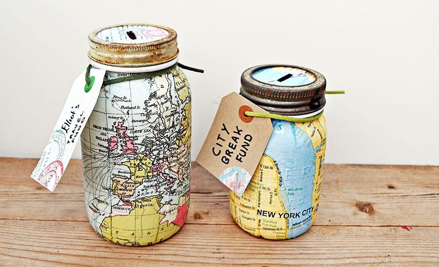 Two mason jar coin banks decoupaged in world map and New York map napkins with luggage tags reading travel fund and city fund