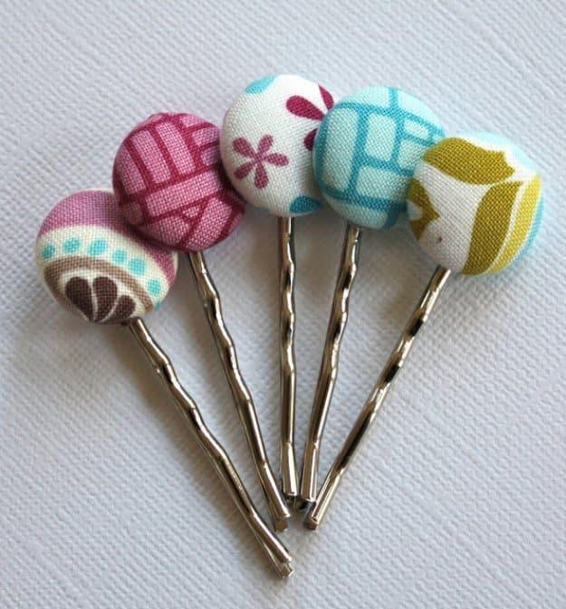 Five fabric covered button bobby pins in pink, teal and mustard prints fanned out on a white textured background