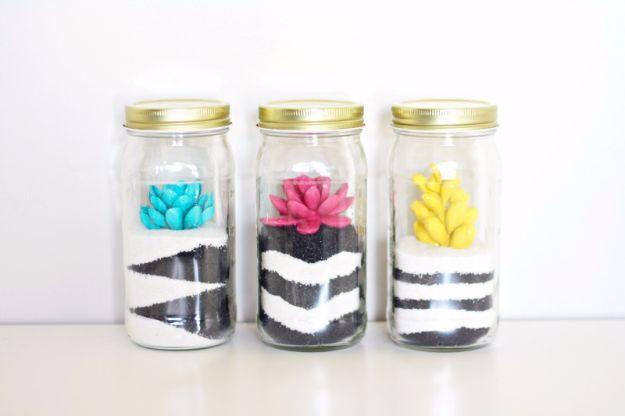 Three jars layered with black and white striped sand, each holding a spray painted succulent in blue or pink