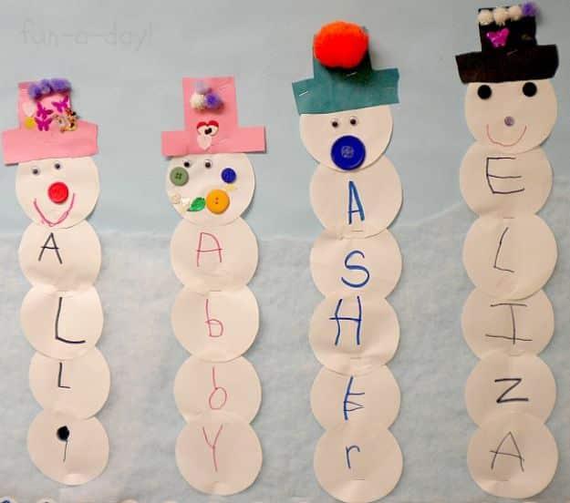 Four paper snowmen made from stacked white circles with a letter on each, topped with paper hats and pom poms