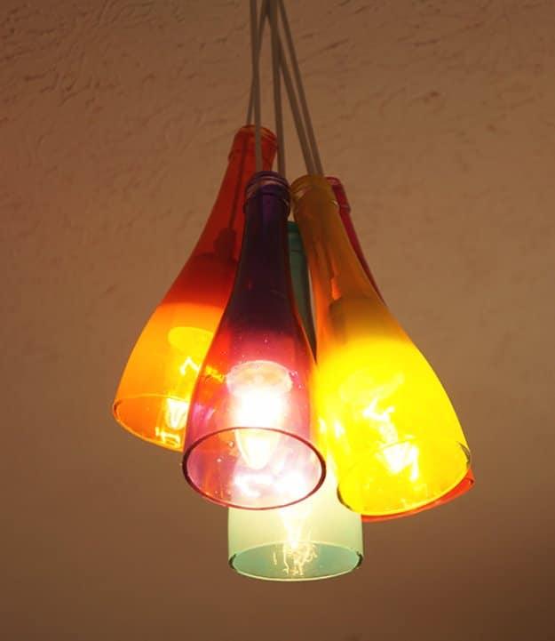 DIY wine bottle chandelier, six cut bottles tinted red, orange, purple and green glowing in a cluster from a ceiling