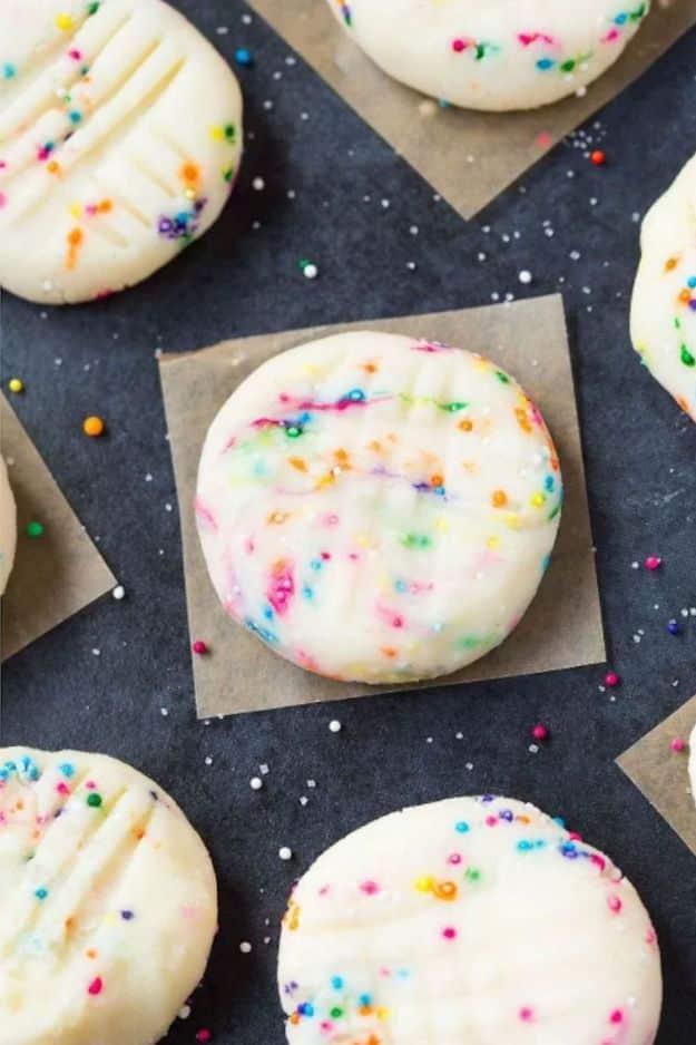 Healthy no bake unicorn cookies, pale round cookies covered in rainbow sprinkles on dark slate and parchment