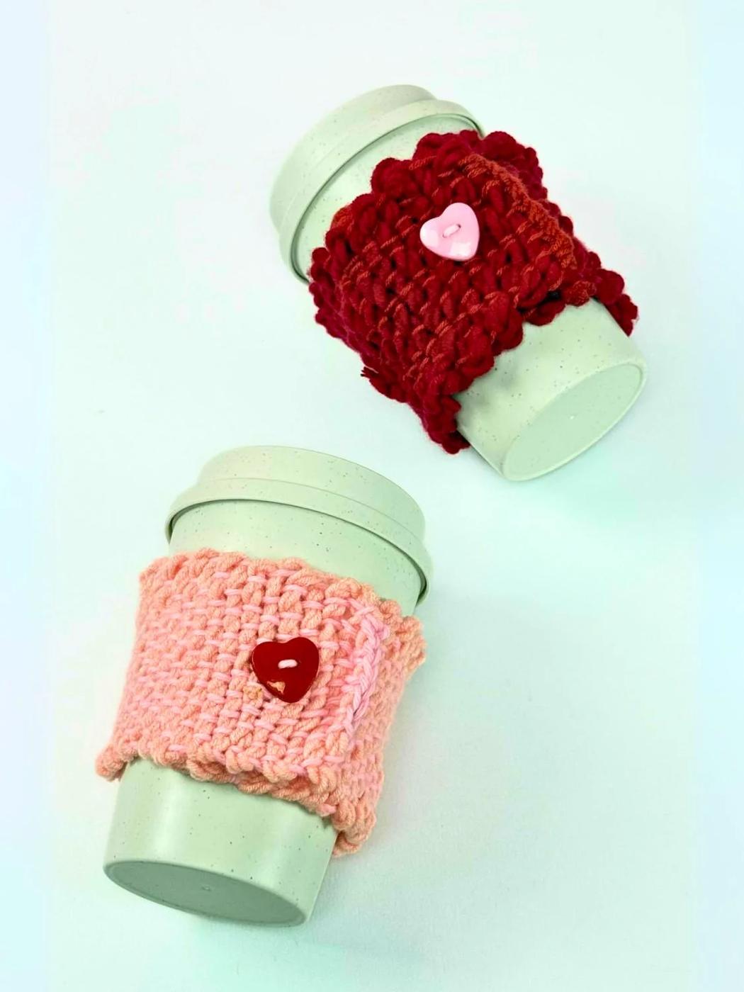 Plain white mug wrapped in a hand woven yarn cozy in cream and mustard stripes, sitting on a light table
