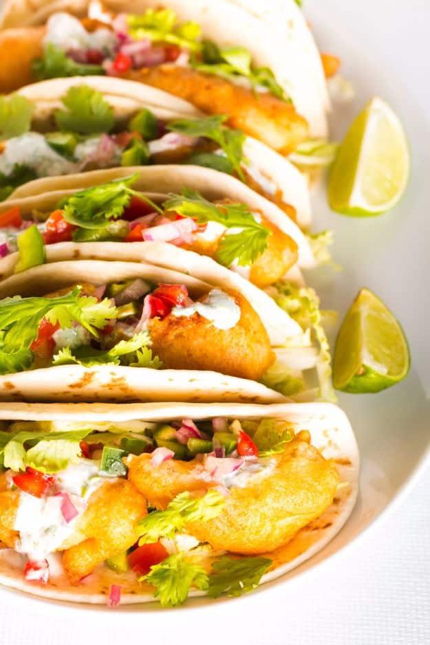 Beer battered fish tacos in soft tortillas with pico and lettuce, stacked on a plate with a lime wedge