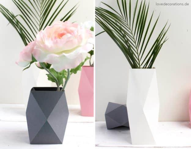 Two faceted folded paper vases in charcoal and white holding a pink rose and palm leaves, with a pink vase behind