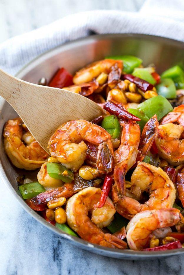 Kung pao shrimp in a skillet with green peppers, peanuts and dried red chilies, a wooden spoon in the pan