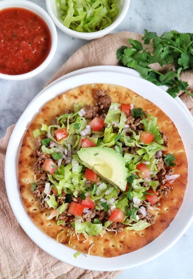Taco pita pizza on a crisp pocketless pita topped with ground beef, cheddar, lettuce, tomato and avocado