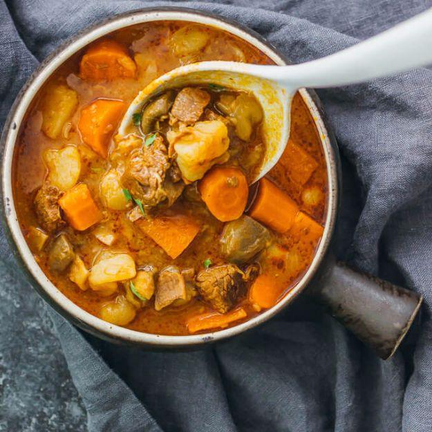 White ladle holding beef, potato and carrot above a handled speckled stoneware pot of instant pot beef stew
