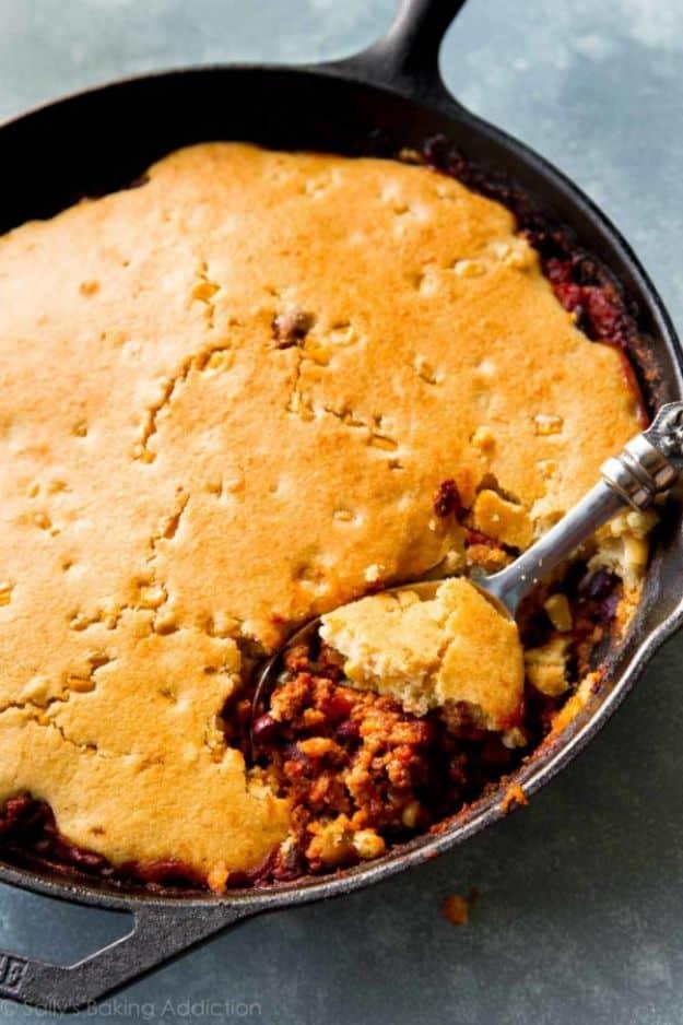 Cast iron skillet chili with a golden cornbread crust baked on top and a spoon lifting out one piece