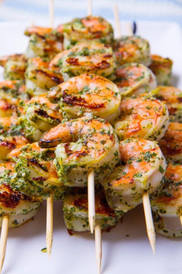 Pesto grilled shrimp on skewers, coated in basil pesto and charred from a medium high grill at a summer cookout