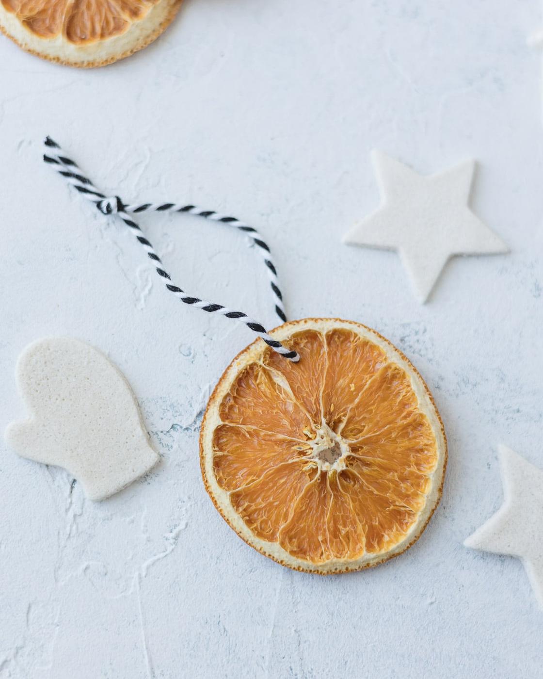A dried orange slice ornament on a black and white twine loop beside white salt dough star and mitten shapes