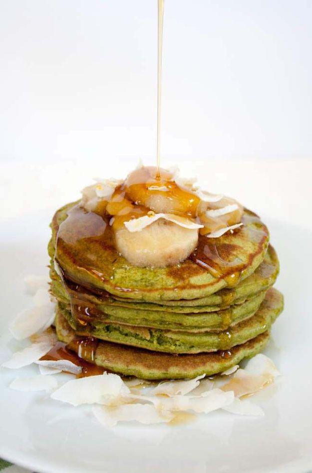 Matcha banana pancakes, a bright green stack topped with caramelized banana, coconut flakes and syrup pouring down