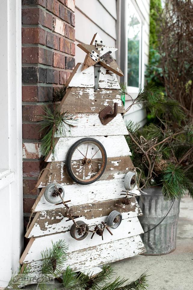 Christmas tree shape built from chippy white reclaimed boards with a wheel rim star, leaning against a brick porch wall
