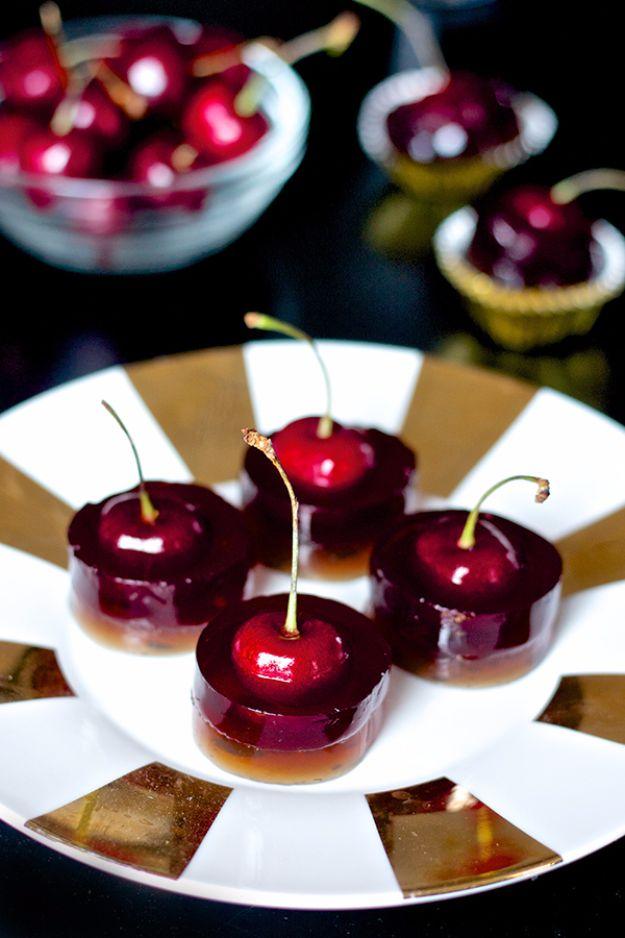 Cherry cola jello shots cut into rounds, each with a whole fresh cherry and stem standing up in the middle