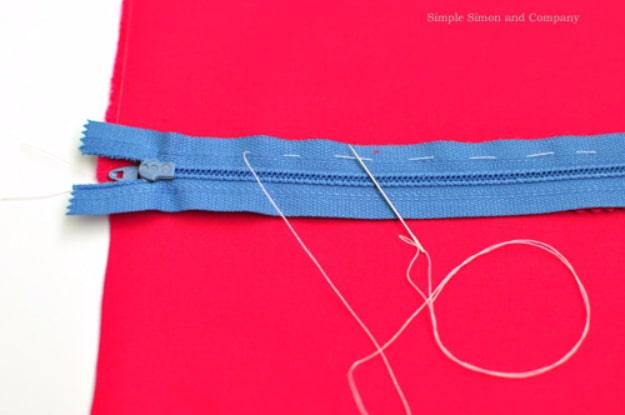 A blue zipper basted onto red fabric with long white running stitches, with a needle and thread alongside