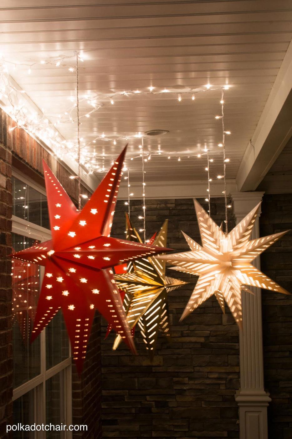 Three large paper star lanterns glowing as they hang from the ceiling of a covered front porch at dusk