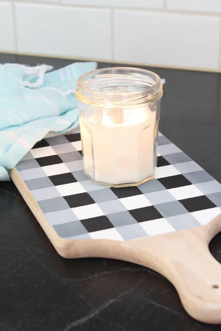 Wood breadboard tray hand painted in a black, gray and white buffalo check pattern holding a lit candle