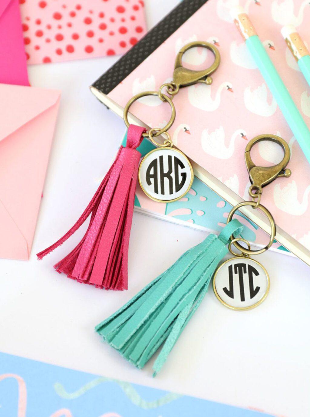 Two monogram bezel keychains with pink and mint suede tassels on gold rings, laid on pink and white stationery