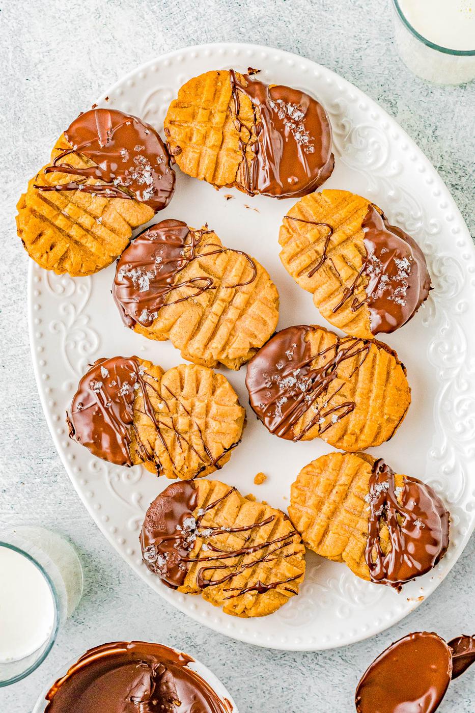 Peanut butter sandwich cookies half dipped in chocolate with a drizzle and flaky salt on a white oval platter