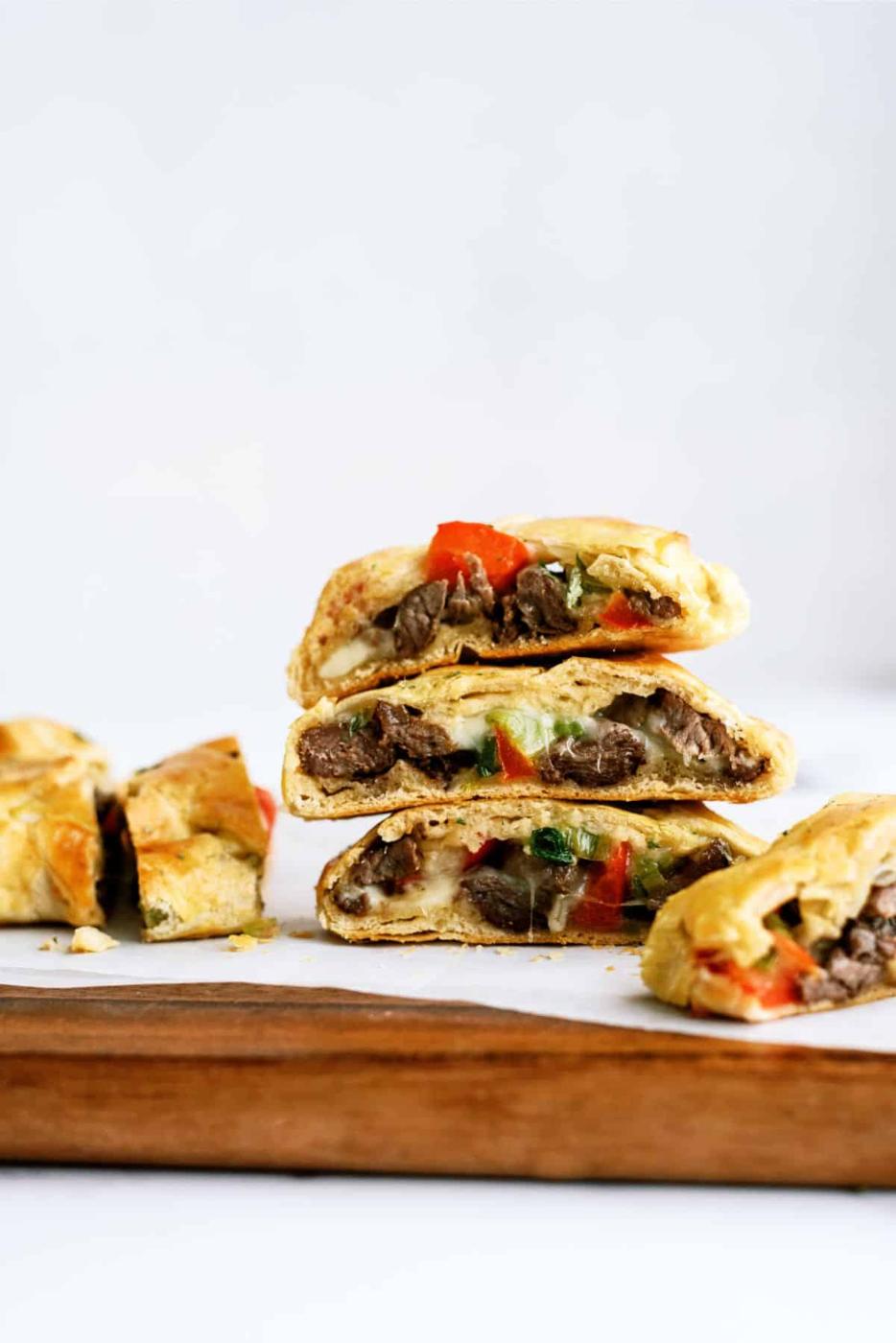 Cheesesteak crescent braid sliced into pieces showing steak, peppers and melted cheese in golden dough