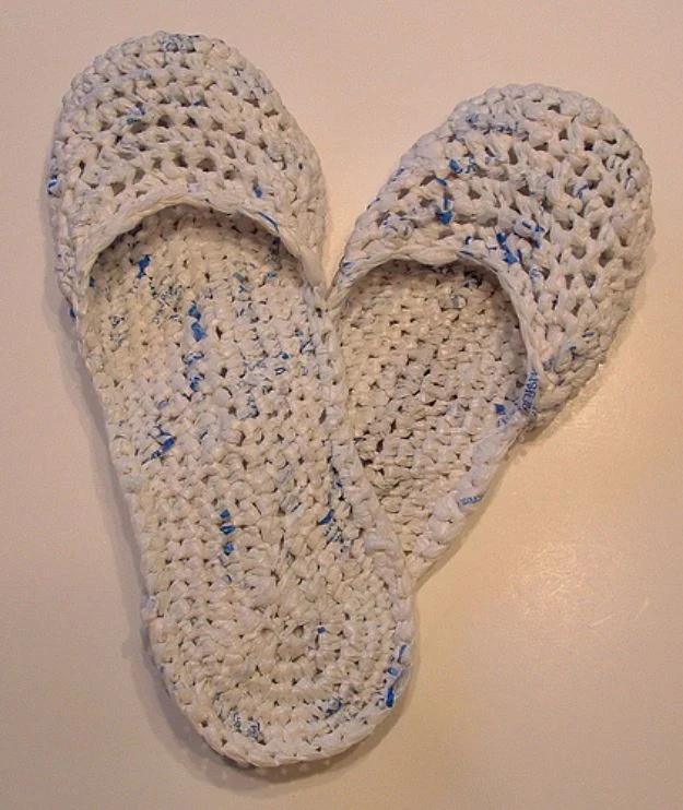 Sandals crocheted from white plastic bag plarn flecked with blue, laid sole to sole in a V on a pale surface