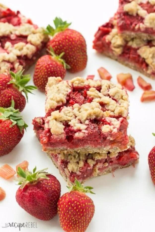 Strawberry rhubarb crumble bars cut into squares on a white surface with fresh strawberries around them
