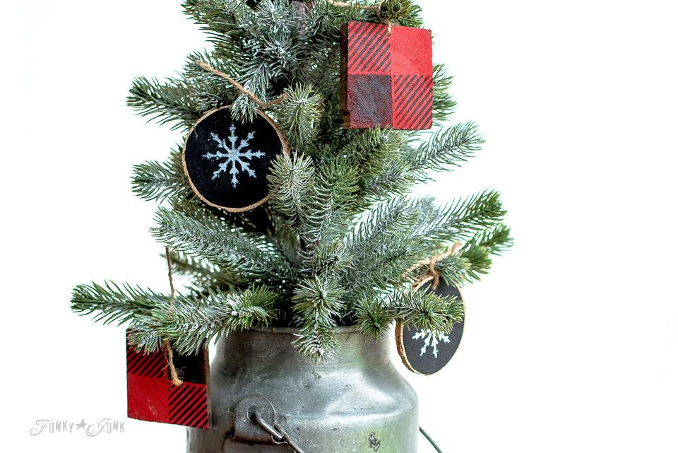 Buffalo check wood block ornaments and black wood slices with white snowflakes hanging on a small flocked tree in a milk can