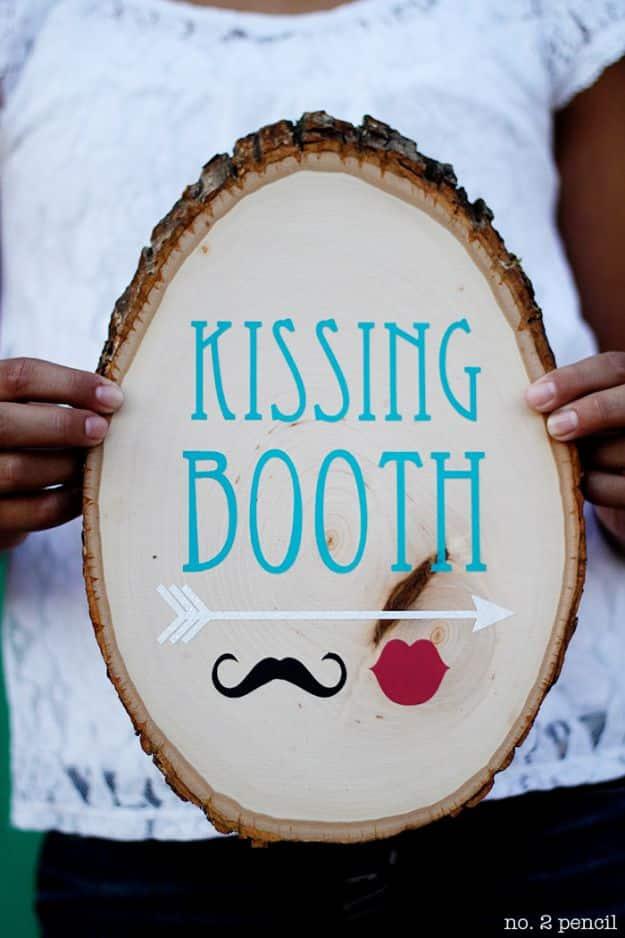 Person holding a bark edged wood slice painted with Kissing Booth, an arrow, a mustache and red lips