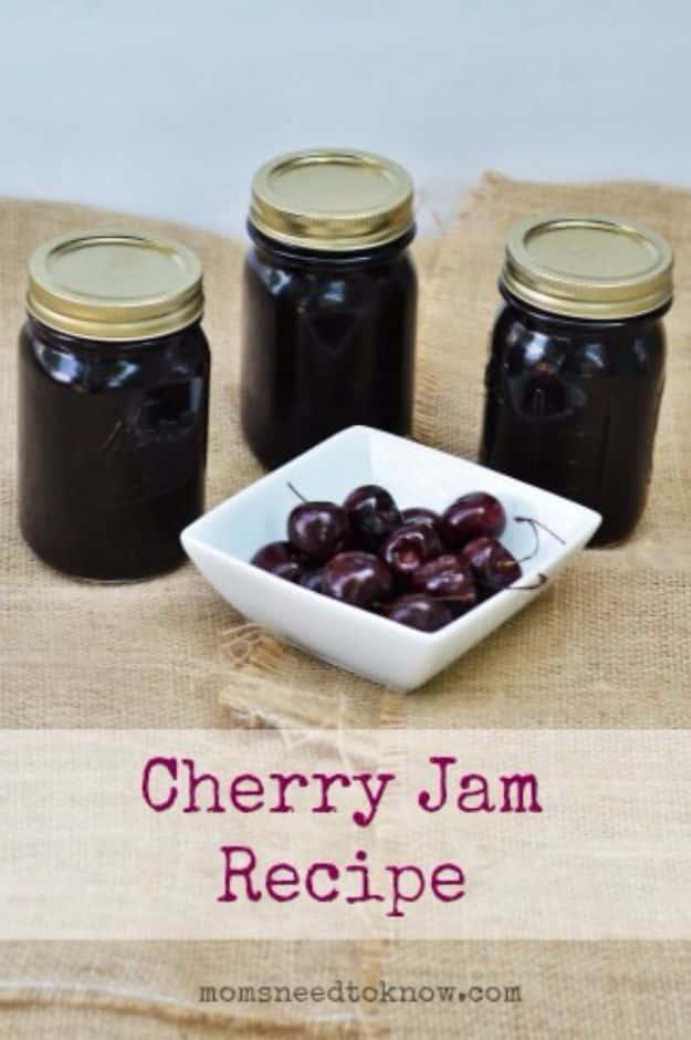 Homemade cherry jam in canning jars, bright red, with fresh pitted cherries and a jar lifter on a counter