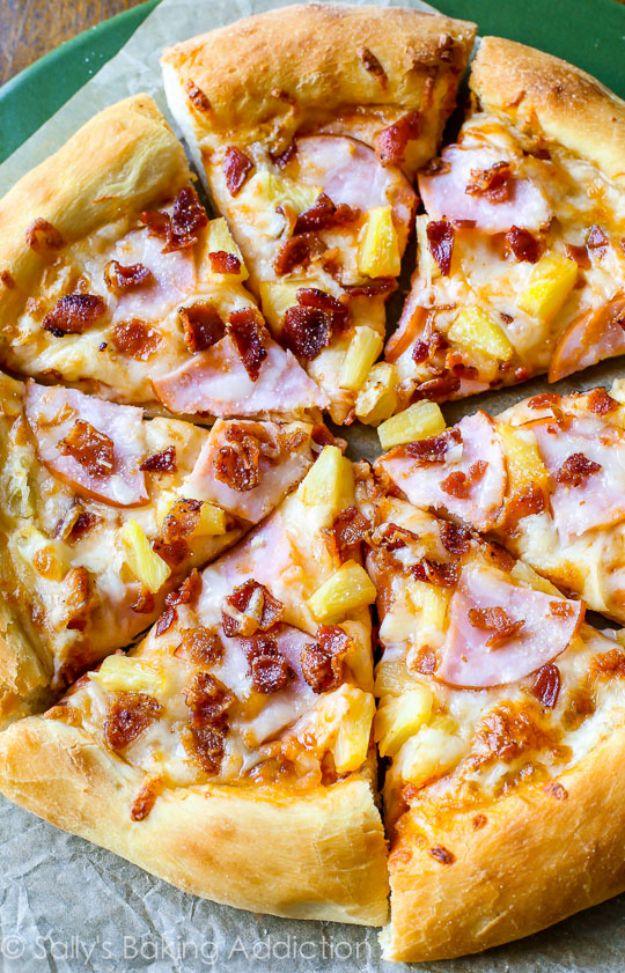 Hawaiian pizza in a green pan with pineapple chunks, cooked ham and crumbled bacon over melted cheese