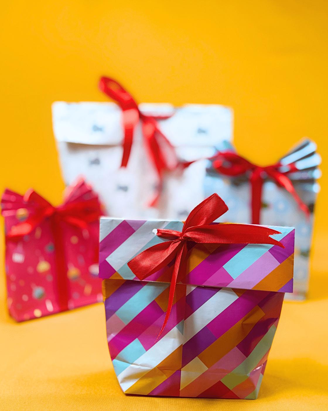 DIY Gift Ideas - three finished wrapping paper gift bags with red ribbons on a yellow backdrop