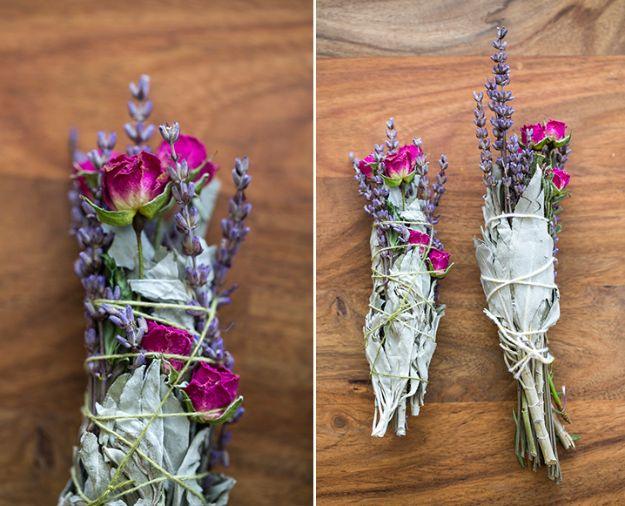 Two bundles of white sage tied with pink roses, lavender and greenery, wrapped in twine on a wooden surface